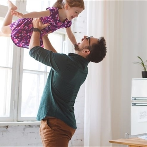 Image of smiling father lifting daughter in kitchen.