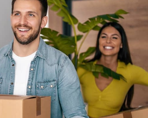 Young couple moving boxes and a houseplant into new home.