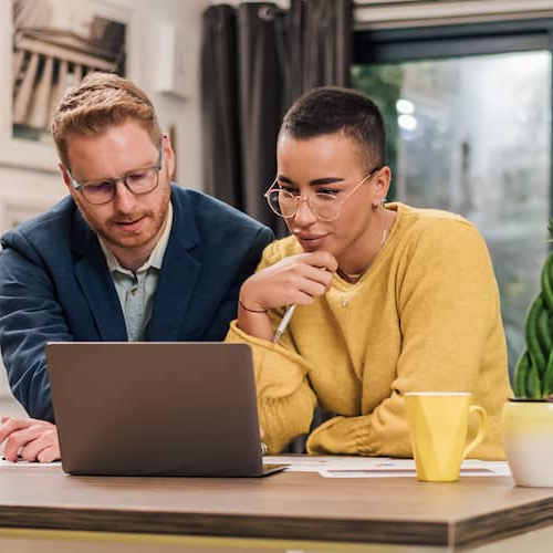 Young couple sitting at a kitchen counter with a laptop, potentially discussing finances or real estate options.