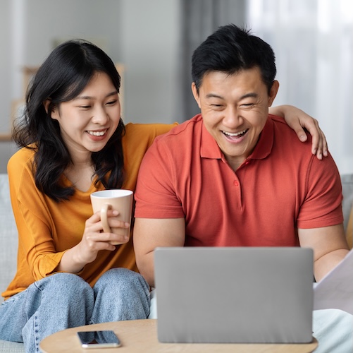 Middle-aged couple looking at computer together while drinking tea or coffee.