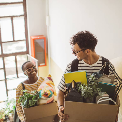 A young couple moving into a new place, carrying boxes.