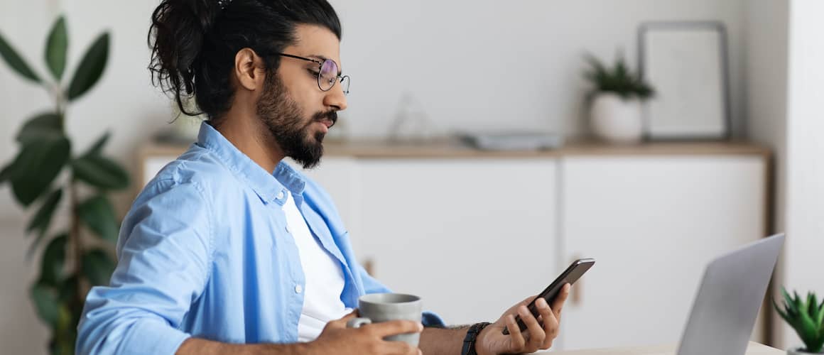 Young man looking at phone holding a cup of coffee.