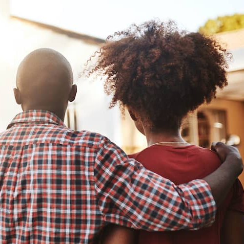 Young couple standing before a new house at sunset.