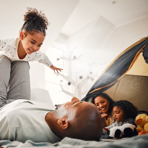 Dad and daughter playing with mother and daughter smiling nearby.