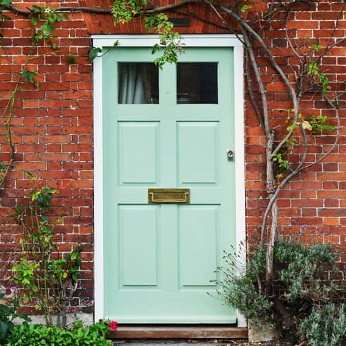 A red brick home front with teal colored door and plant vines.