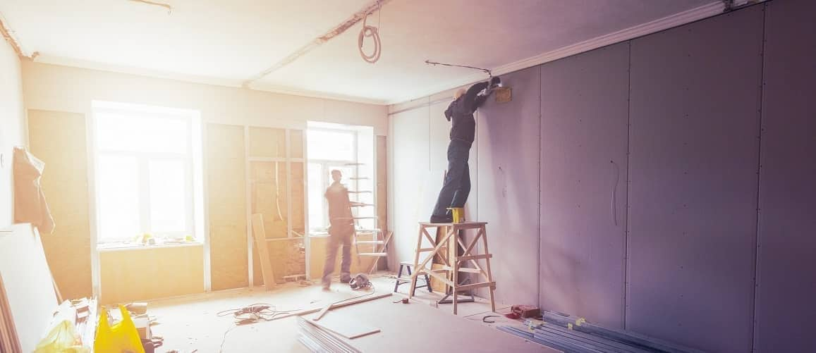 Two men fixing drywall, potentially illustrating renovation or repair work being done inside a house.