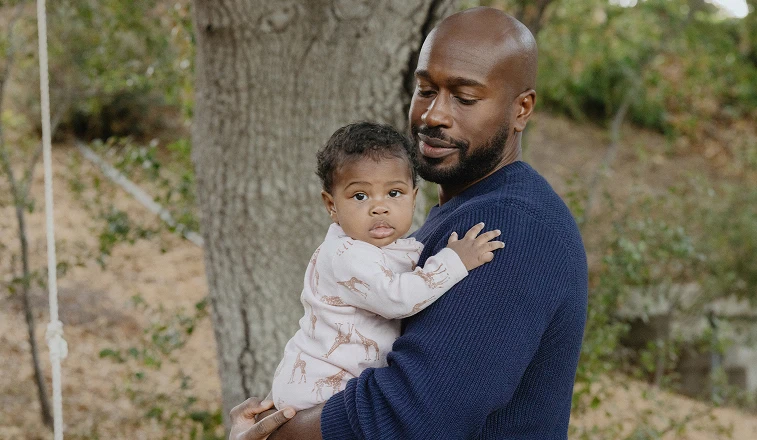 A man looks down lovingly at the infant in his arms.