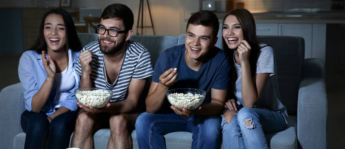 Group of friends watching TV with popcorn and pizza.