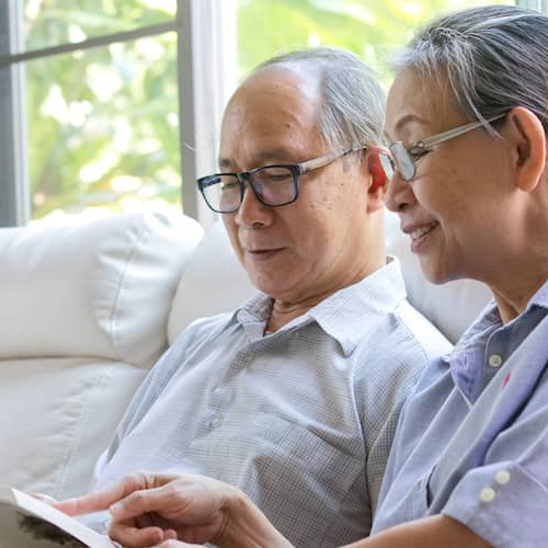 An older couple on a couch with a book, depicting relaxation or leisure time at home.