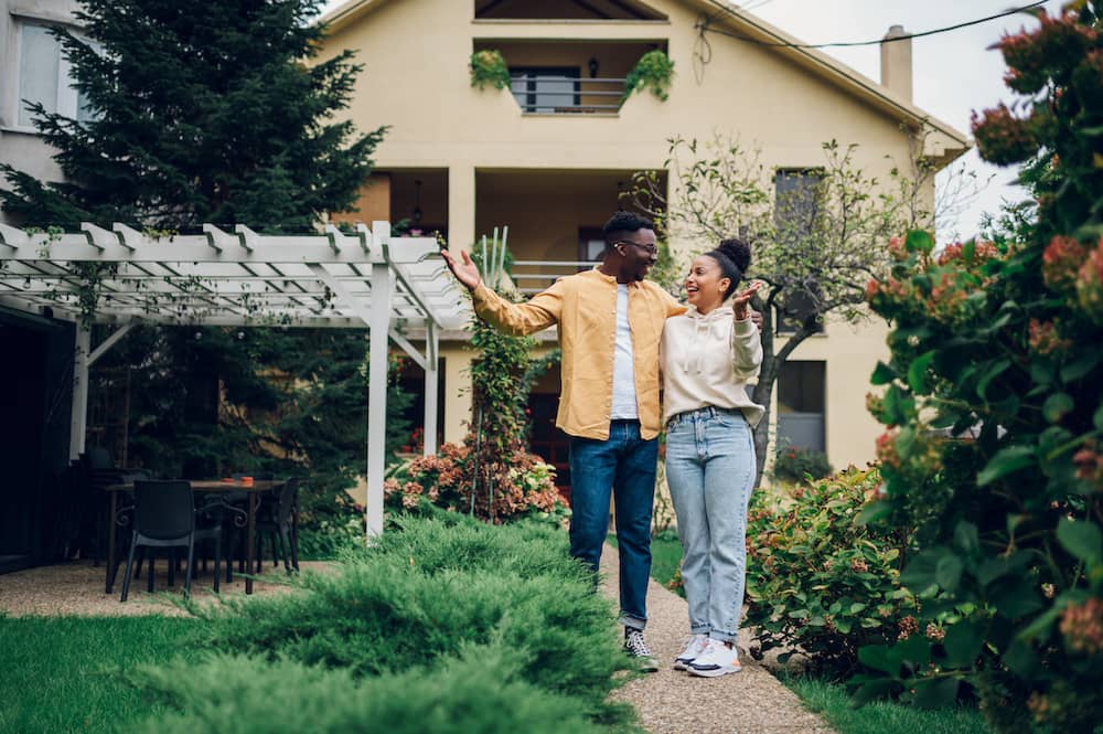 Couple with arms around each other, smiling, in front of new home.