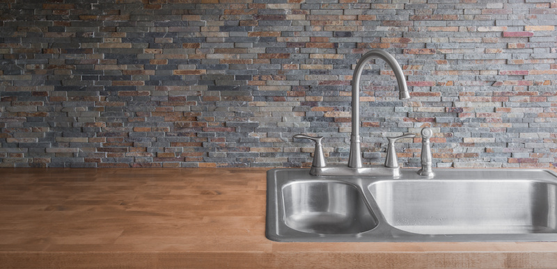 Wooden countertop with a modern stainless steel sink and faucet and a stone tile backsplash.