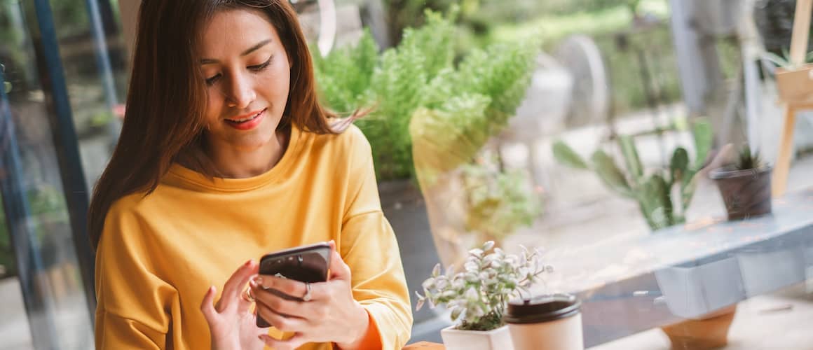 Woman in yellow shirt on her phone checking her credit score.