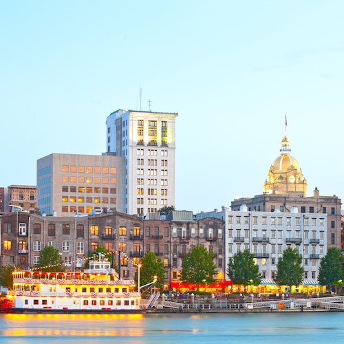 Savannah Georgia USA, skyline of historic downtown at sunset with illuminated buildings and steam boats.