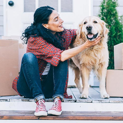A woman petting her dog surrounded by cardboard boxes possibly indicating recent move to her new home.