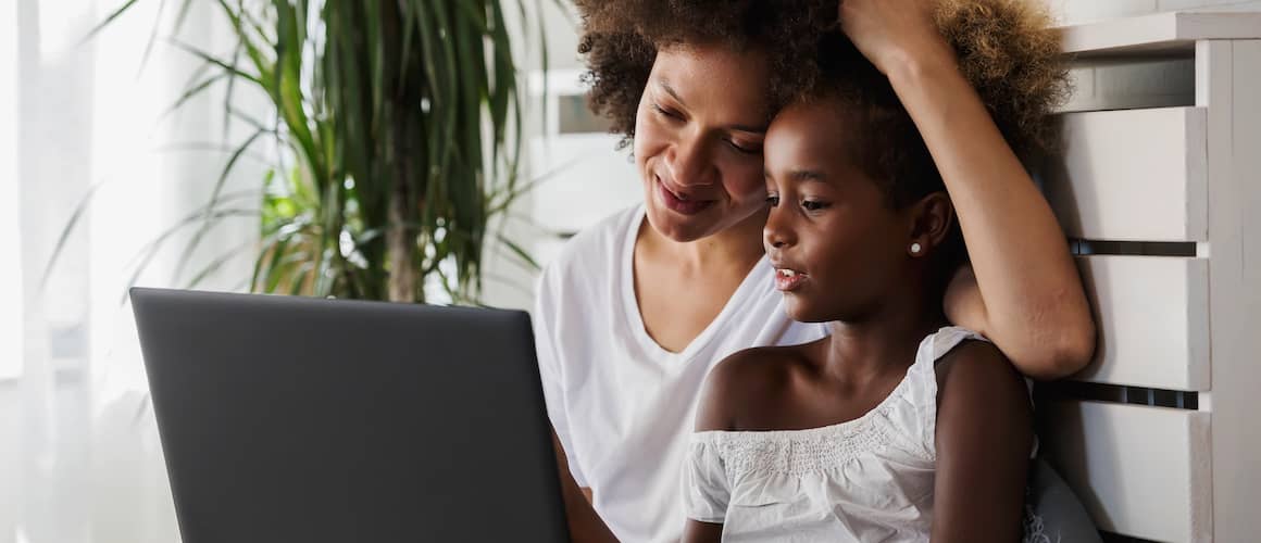 A woman and child sitting on a couch, engrossed in a laptop.