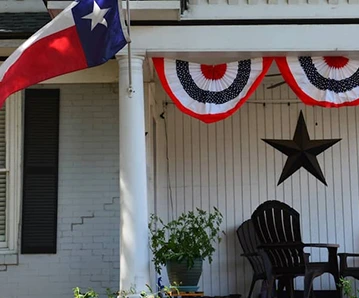 Una casa en Texas con un porche delantero, una bandera de Texas y una estrella en la casa.