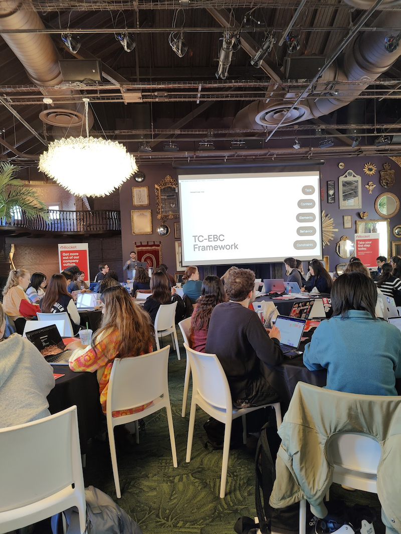 Conference room with groups in tables watching presentation.