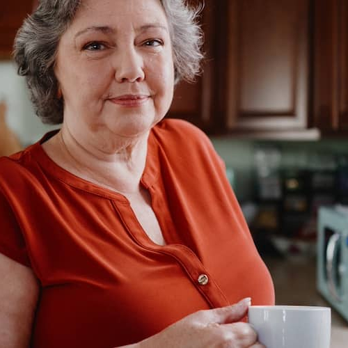 Woman in kitchen holding a cup of coffee.
