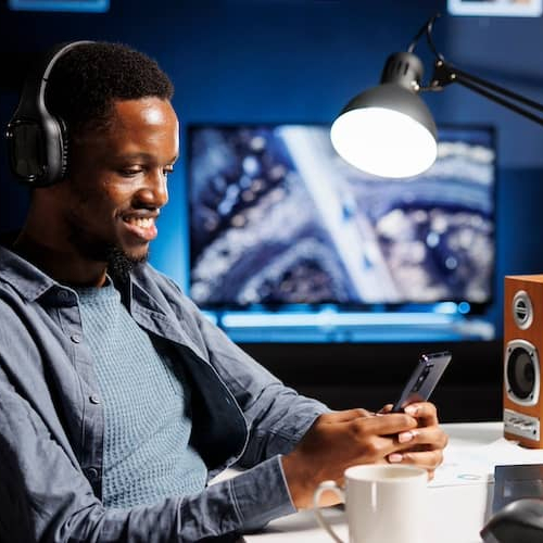Young man sitting at his desk and smiling while using his smart phone.