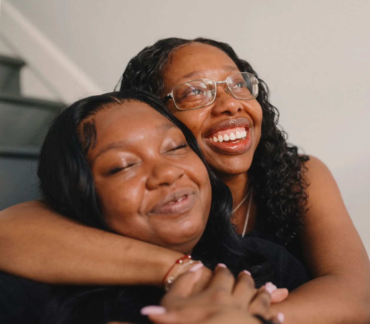 A Black mother and daughter hug by the staircase of their new home.