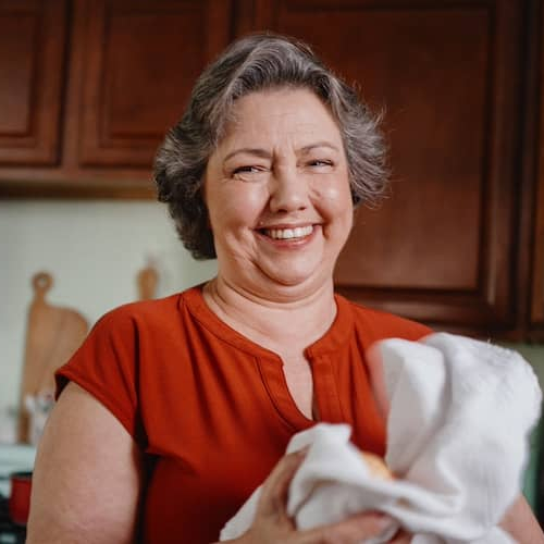 Woman in kitchen, drying dishes and smiling.