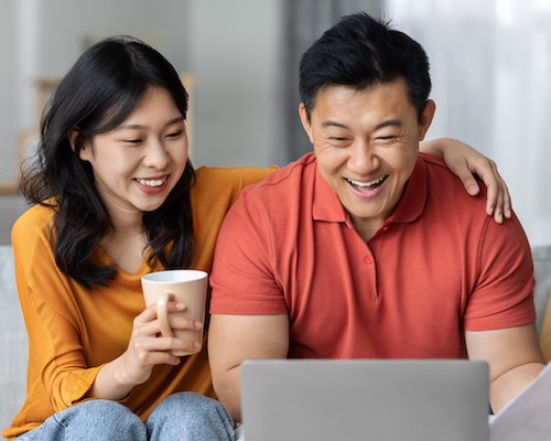 Middle-aged couple looking at computer together while drinking tea or coffee.