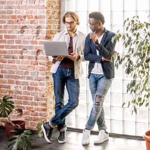 Couple looking at open laptop standing up in loft with housepants and exposed brick wall.