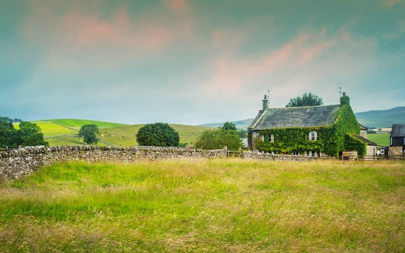 English cottage with climbing greenery and lush, green fields and rolling hills. 