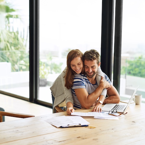 Couple looking at finances in their home while snuggling.