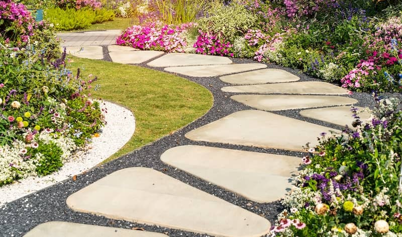 Pathway of dark gray stones with large pavers through garden.