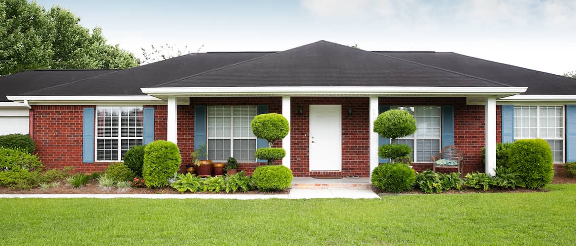 A single storey red brick house with a green front yard.