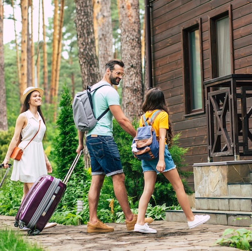 Family with suitcases about to walk up the steps for a vacation rental home in a forested area,