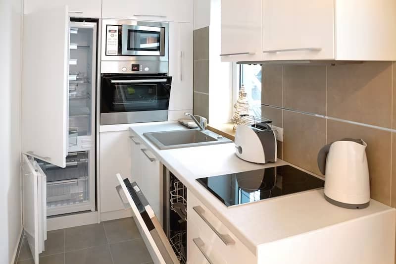 Tiny home kitchen featuring modern, white, sleek finishes and cabinets and high end appliances.