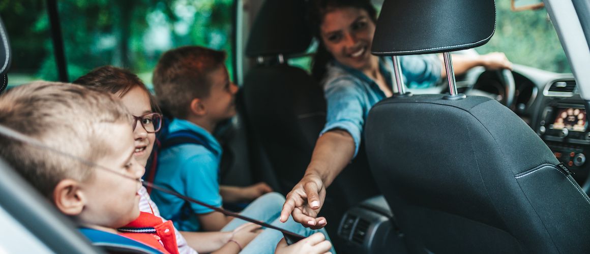 Image of mom buckling children into backseat of car.