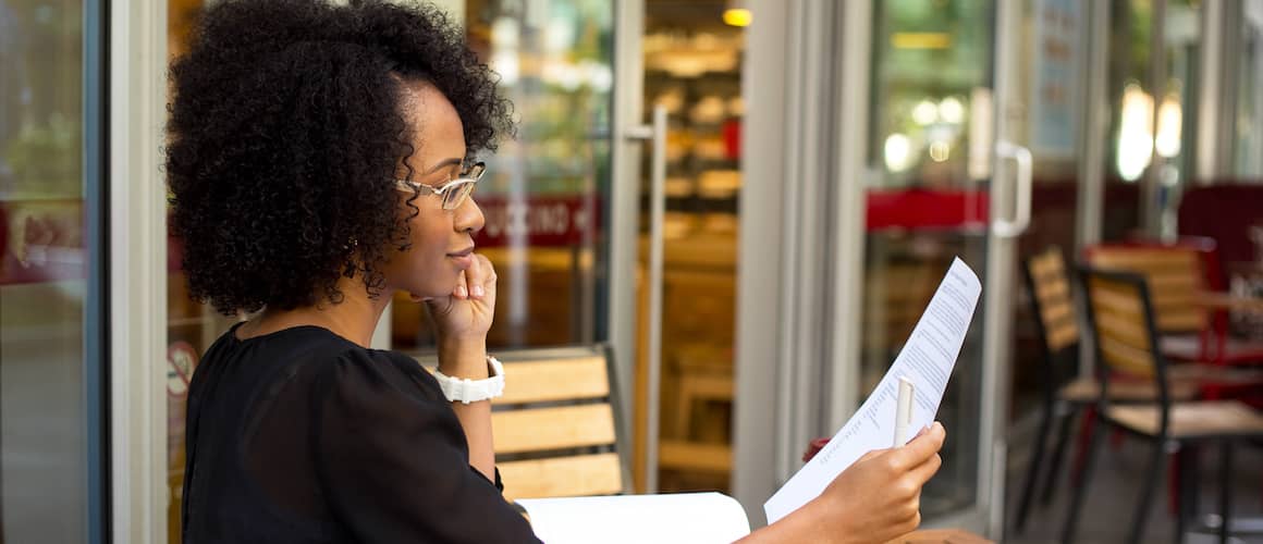 Young African American woman reading a document outside a cafe.