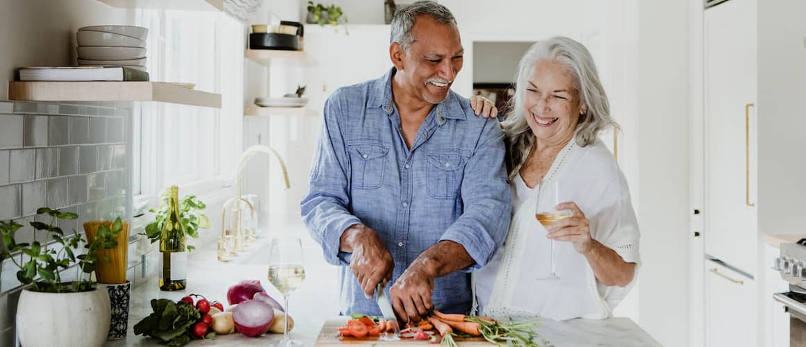 Retired couple smiling and cooking together in their kitchen.