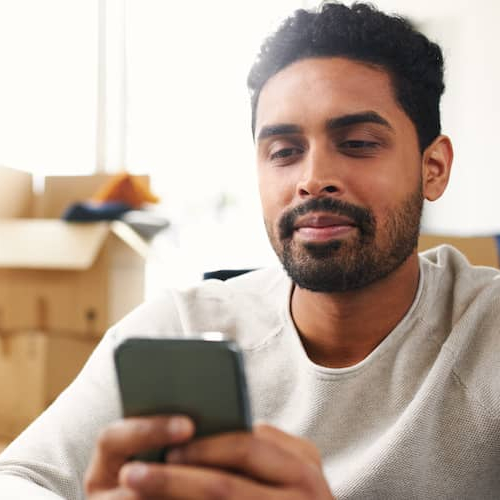 A person looking at his phone surrounded by boxes indicating he just moved into a new house or apartment.