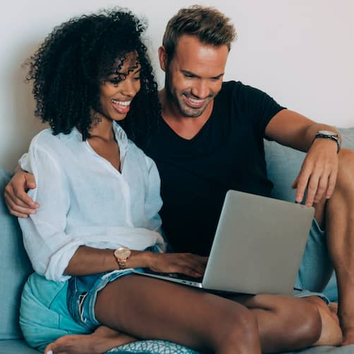 A couple looking at some information on their laptop while sitting on their home couch.