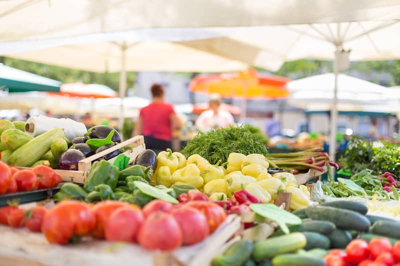 RHB Assets From IGX: Vibrant farmers' market stall with fresh produce and smiling vendor.