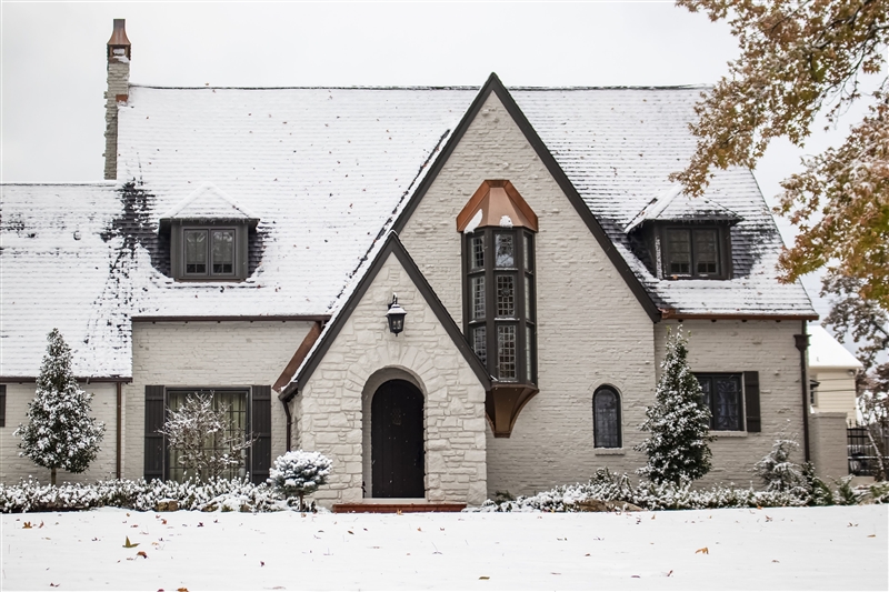 White brick Tudor style home covered in snow in winter.