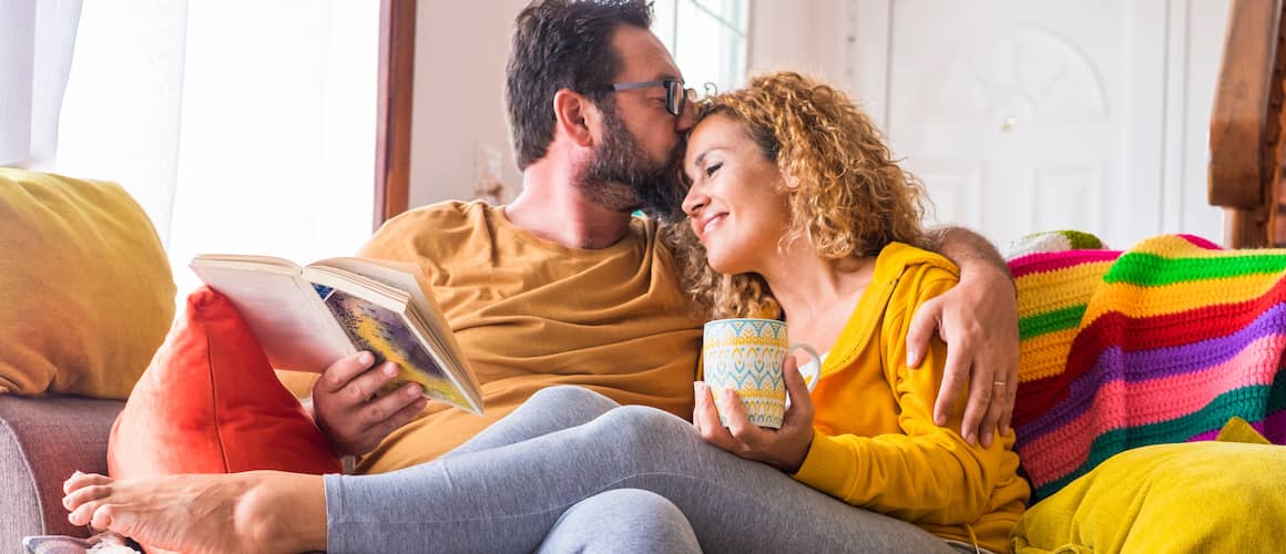 A happy couple reading and drinking coffee on a couch, likely depicting leisure or relaxation at home.