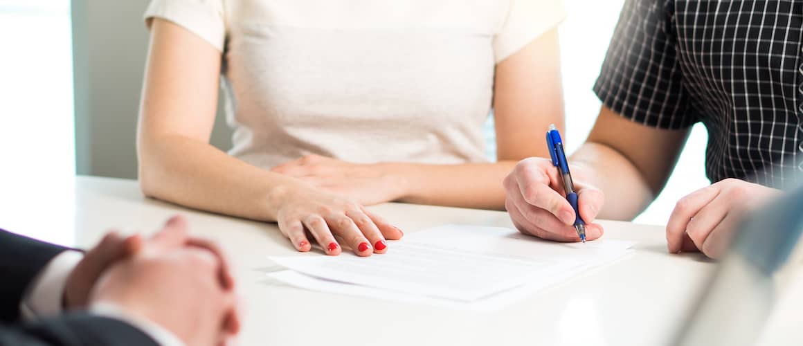 Young couple signing a contract together at an office.