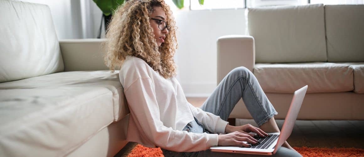 Woman sitting against couch, reviewing loan offers on computer.