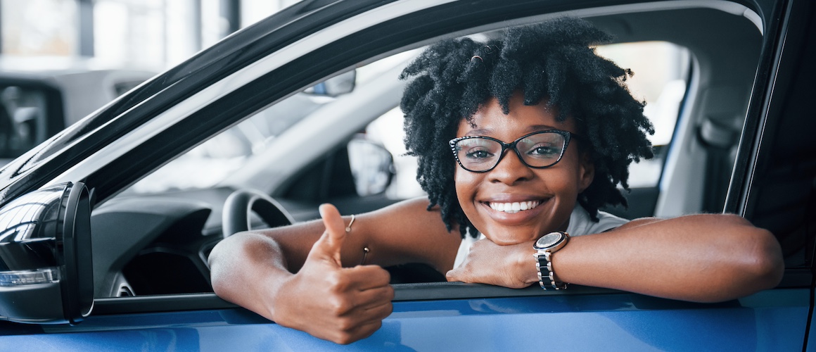 Young African American woman sits inside of new modern car thumb up