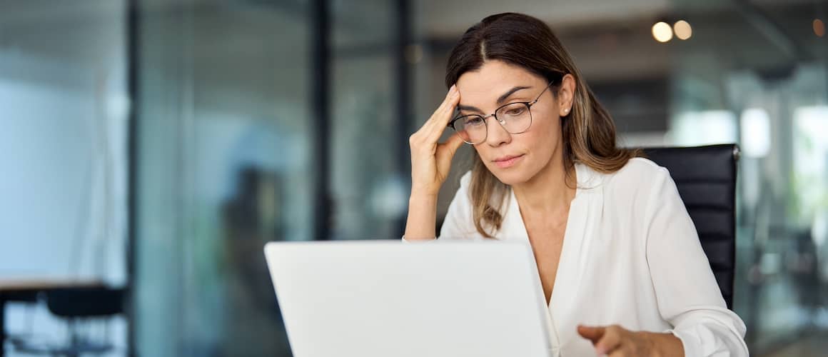 Woman touching her forehead and looking at computer screen with worried look on her face.