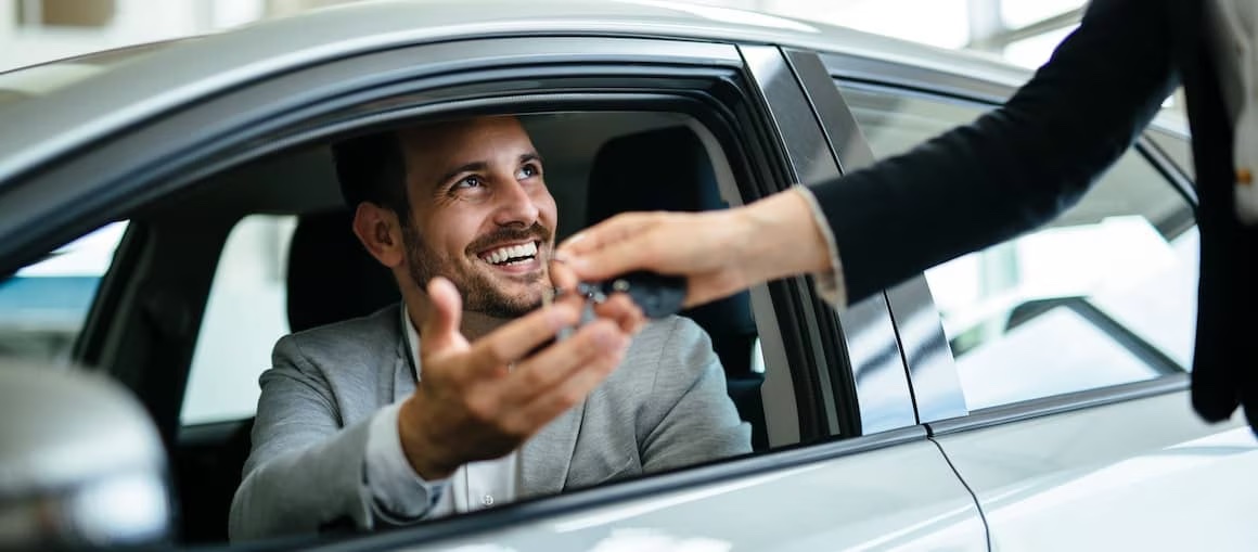 Man receiving keys while sitting in front seat of new car.