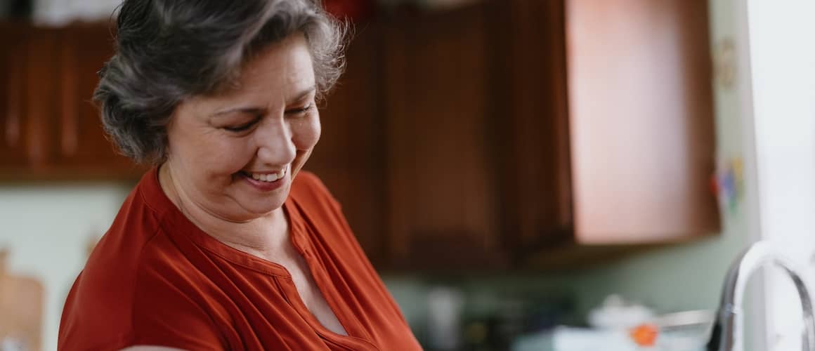 Woman doing dishes in her kitchen, smiling.