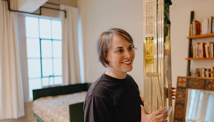 Person with arm tattoos wearing a black shirt and holding a ladder with a green top.