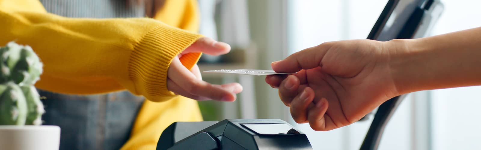 Person wearing yellow sweater, reaching out to take credit card offered by another.