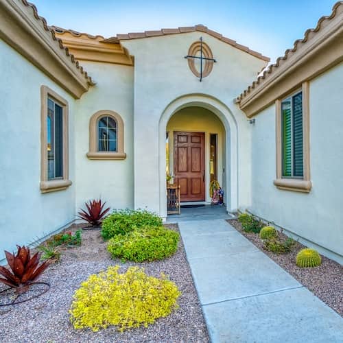 Southwest style white stucco home with Spanish style tiled roof and rounded doorway and windows. Landscape is drougt resistant.